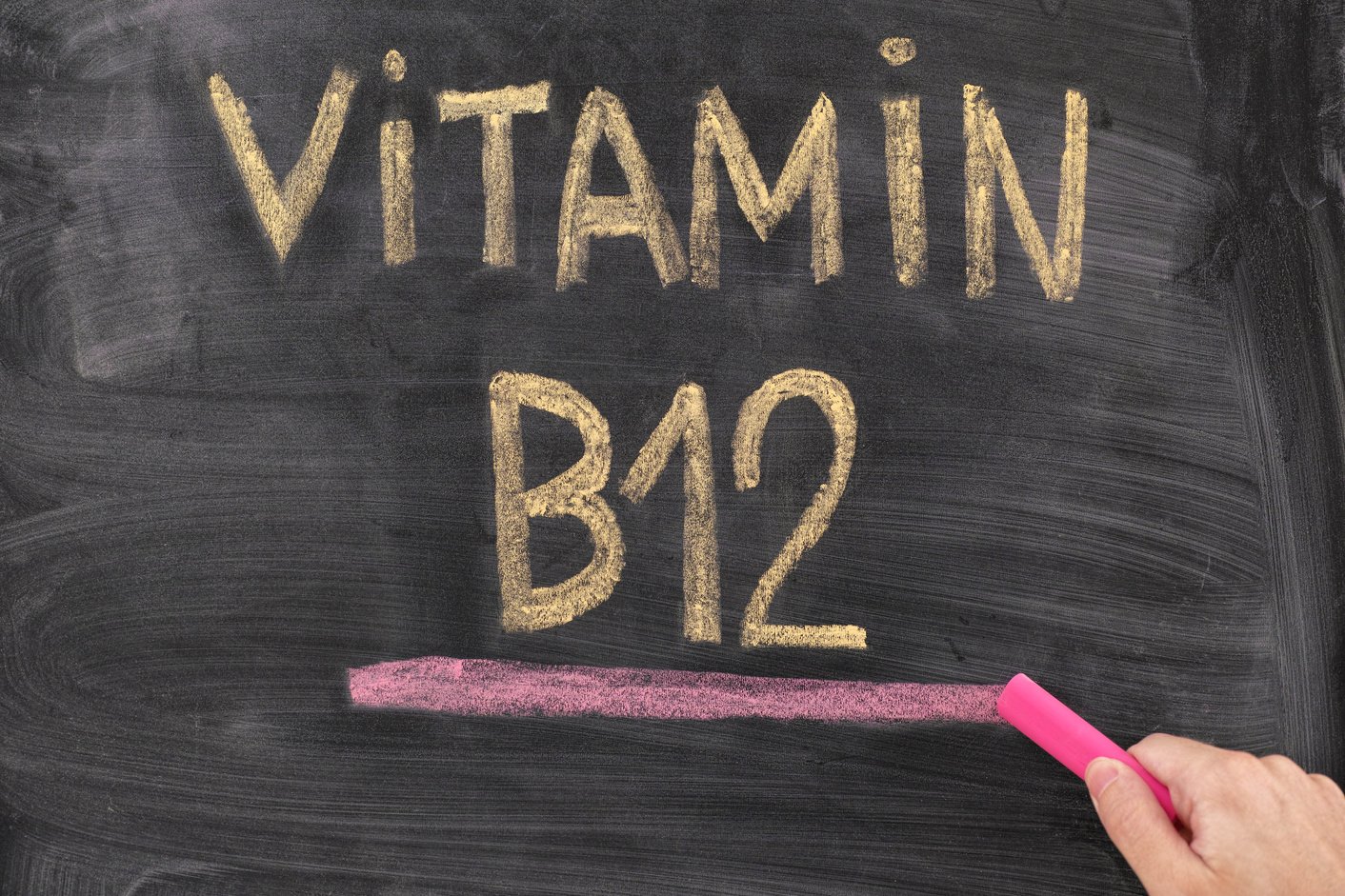 Man writing words Vitamin B12 on chalkboard